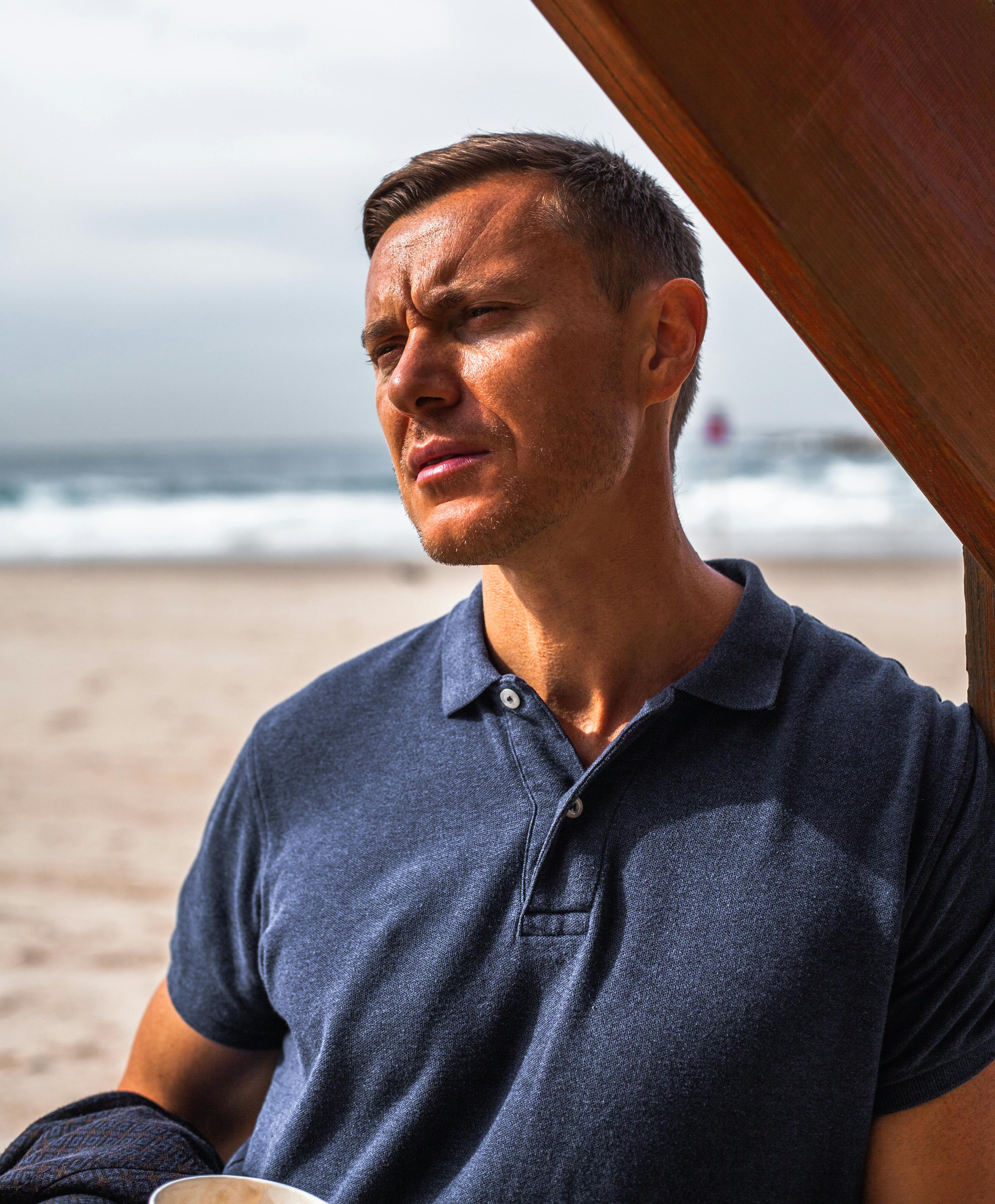 A thoughtful man in a polo shirt stands by the sea in Tel Aviv, Israel.