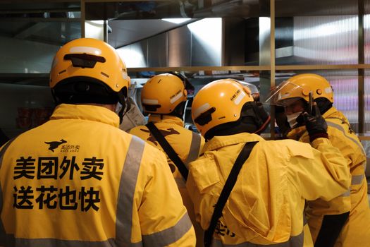Group of delivery workers wearing yellow uniforms and helmets indoors.