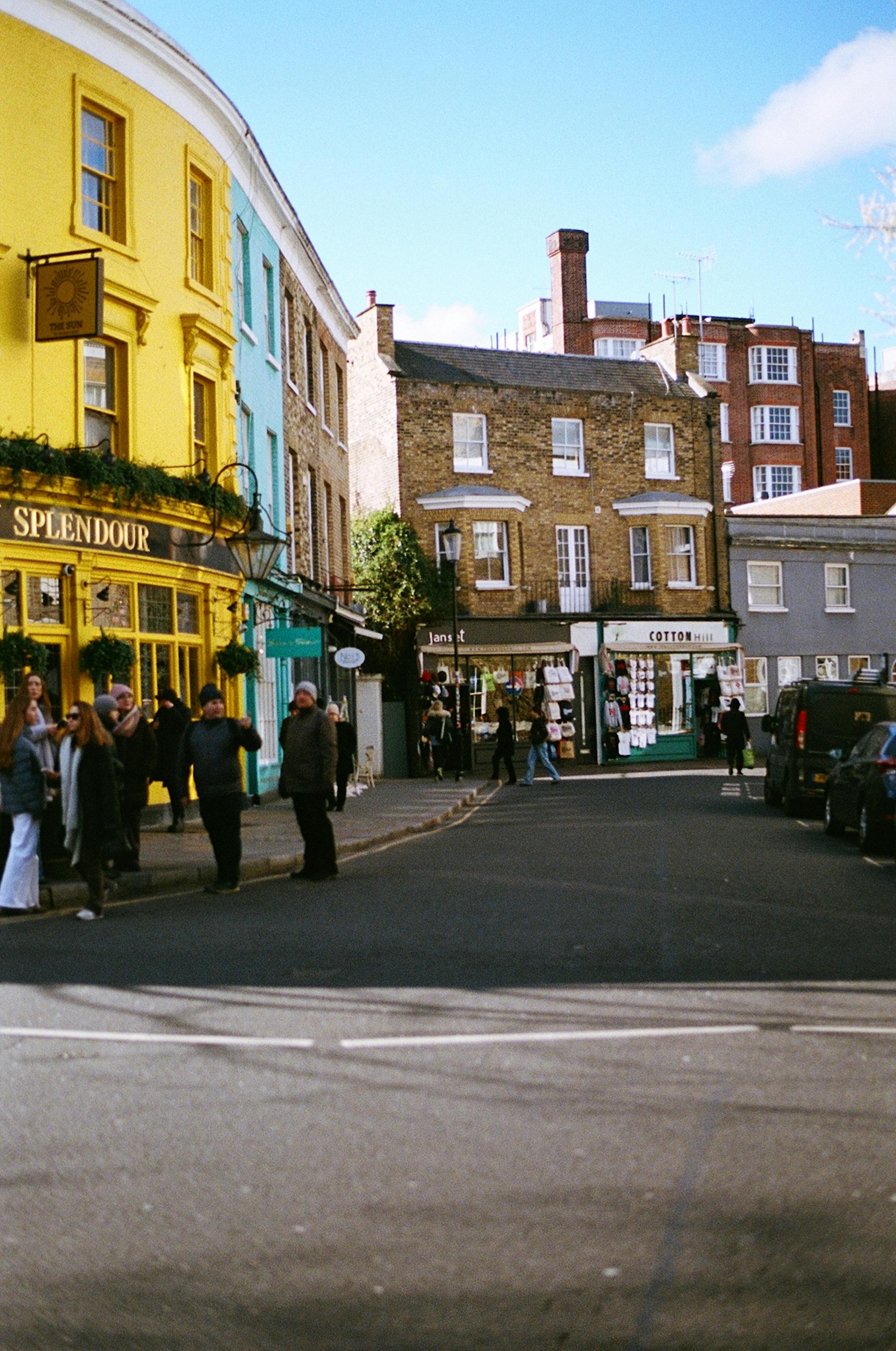 A lively downtown street scene featuring colorful buildings, shops, and people enjoying a sunny day.