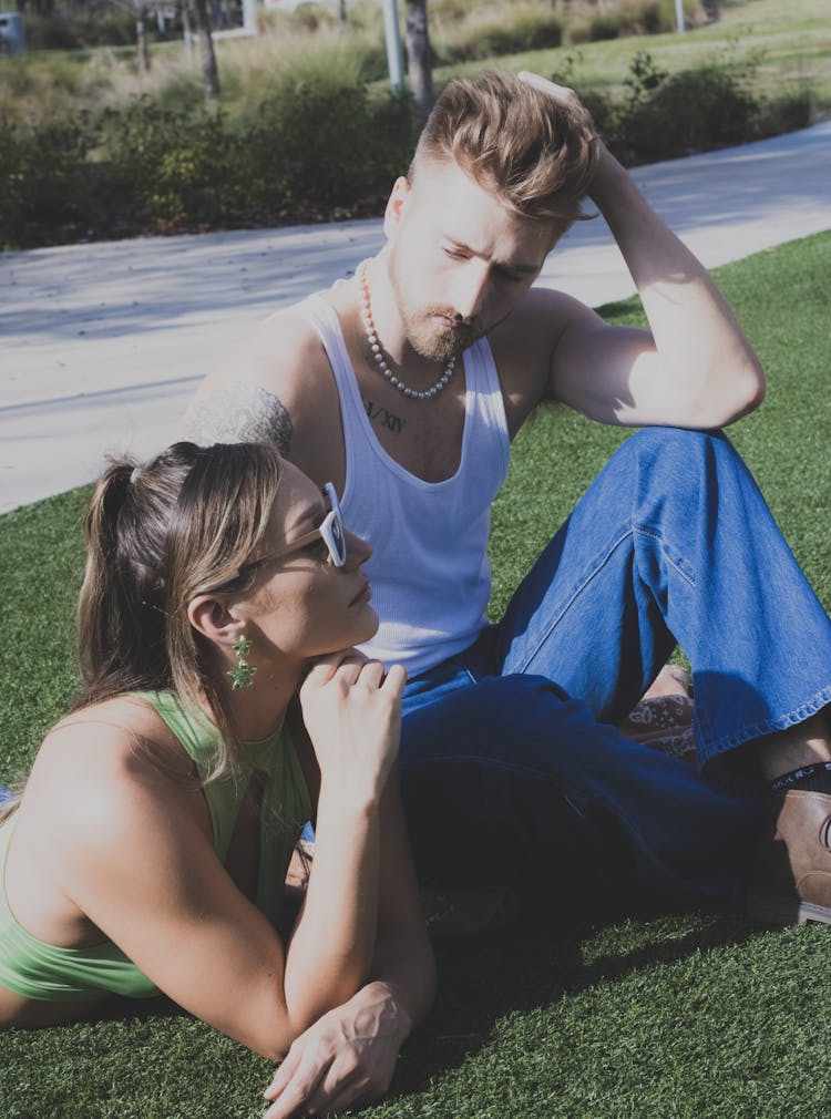 Young Man And Woman In Summer Outfits Sitting On The Grass 