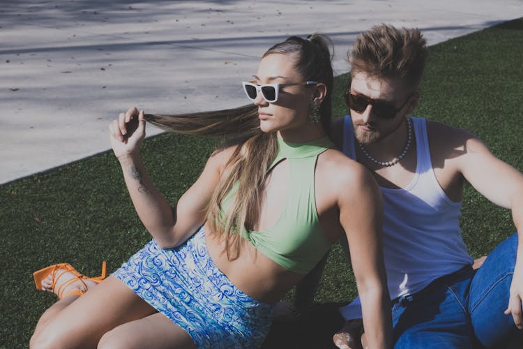 Young Man And Woman In Summer Outfits Sitting On The Grass 