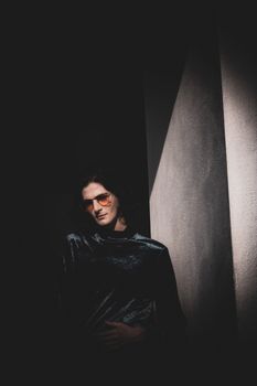 Dark, artistic portrait of a man in sunglasses against a textured wall.