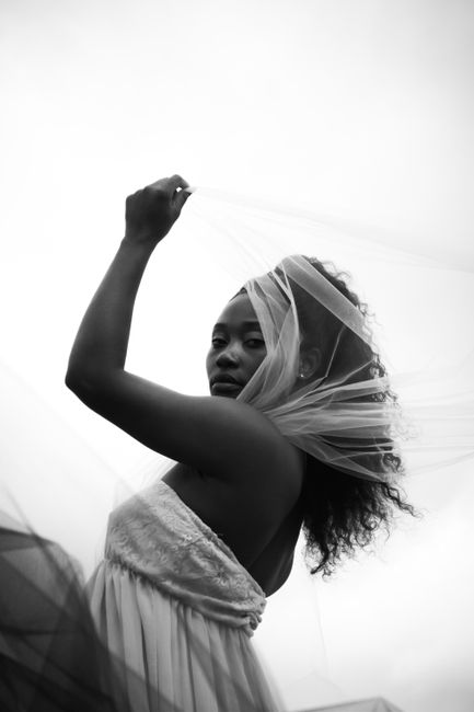 Black and white portrait of a young woman posing outdoors, elegantly draped in a delicate veil.