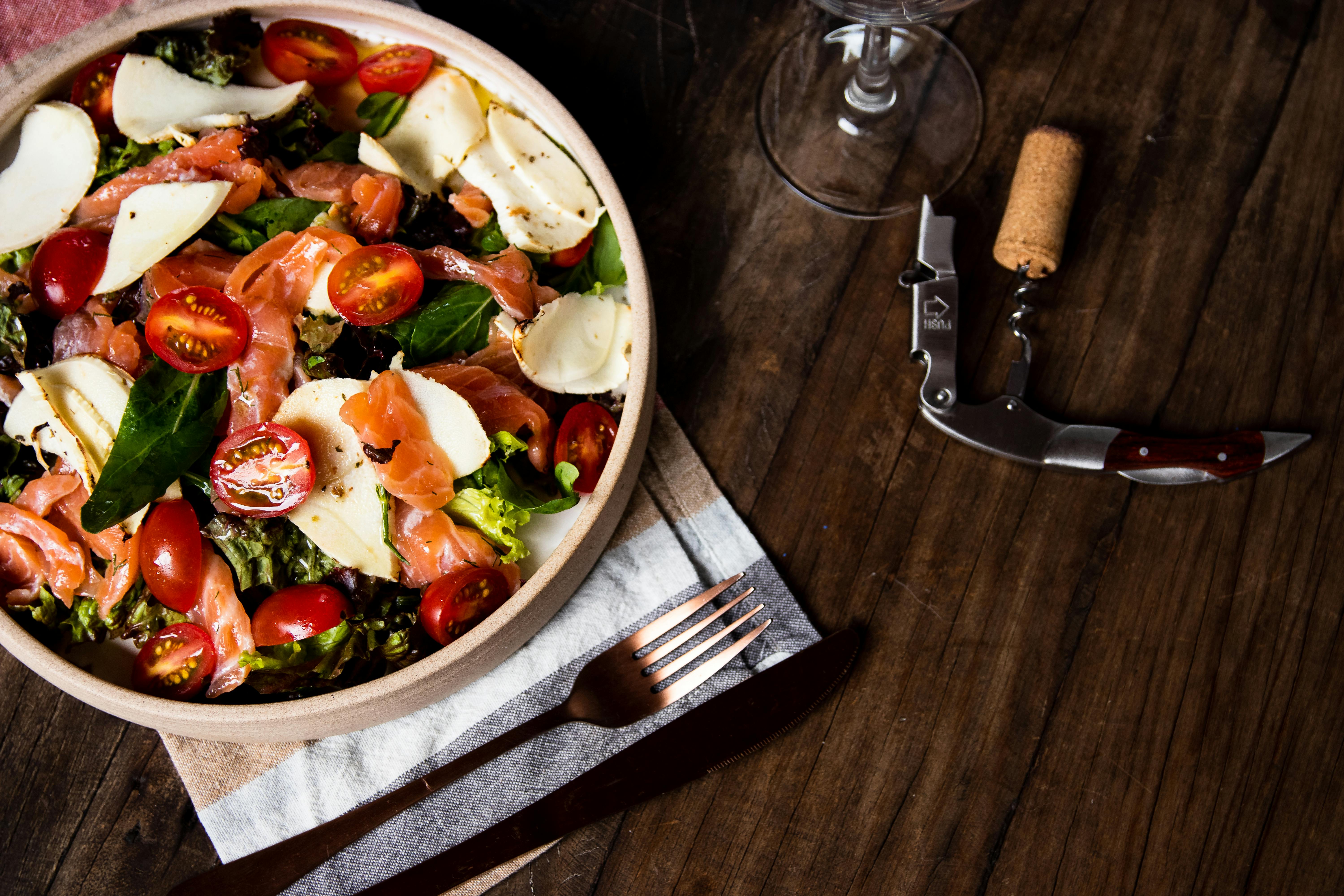 A delicious fresh salad with salmon, mozzarella, and cherry tomatoes on a rustic wooden table.