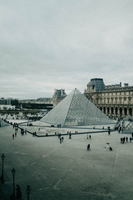 Aerial view of the Louvre Pyramid and courtyard with people on a overcast day.