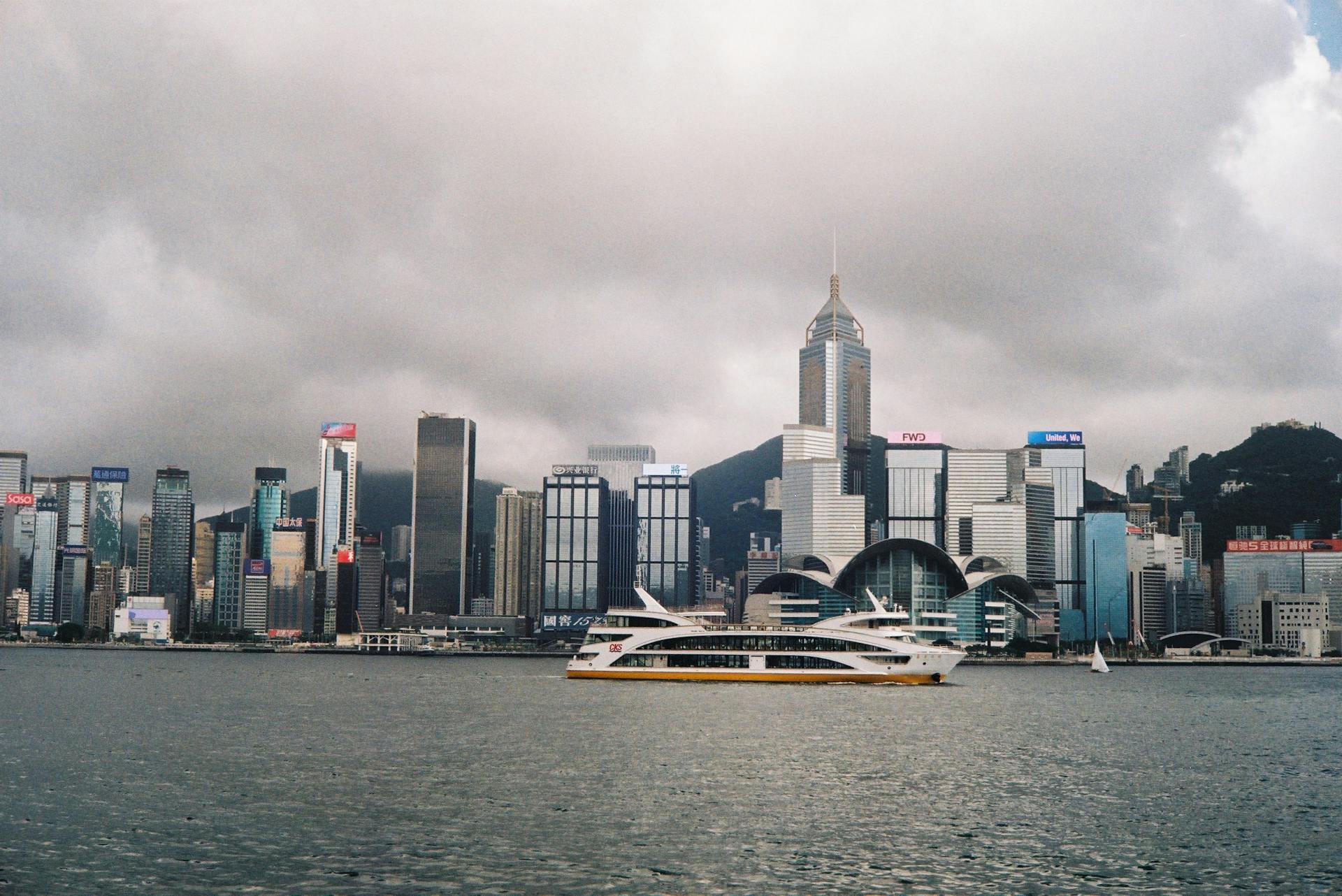 Scenic view of Hong Kong skyline and ferry in Victoria Harbour under cloudy sky.