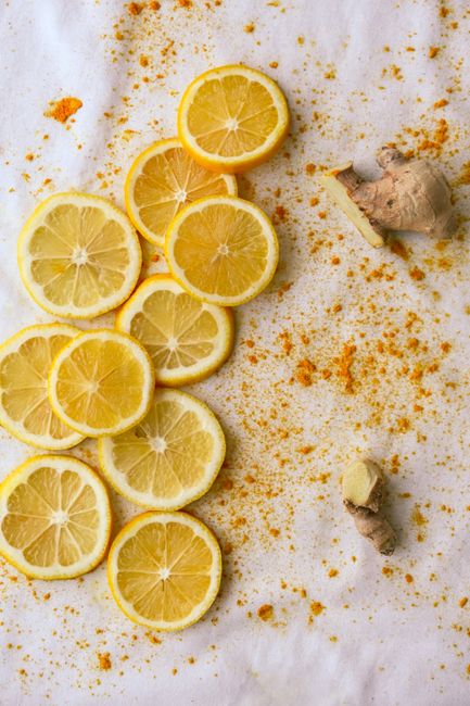 Small glass shot bottles filled with bright orange turmeric liquid, garnished with a slice of fresh ginger and a wedge of lemon on a wooden tray.