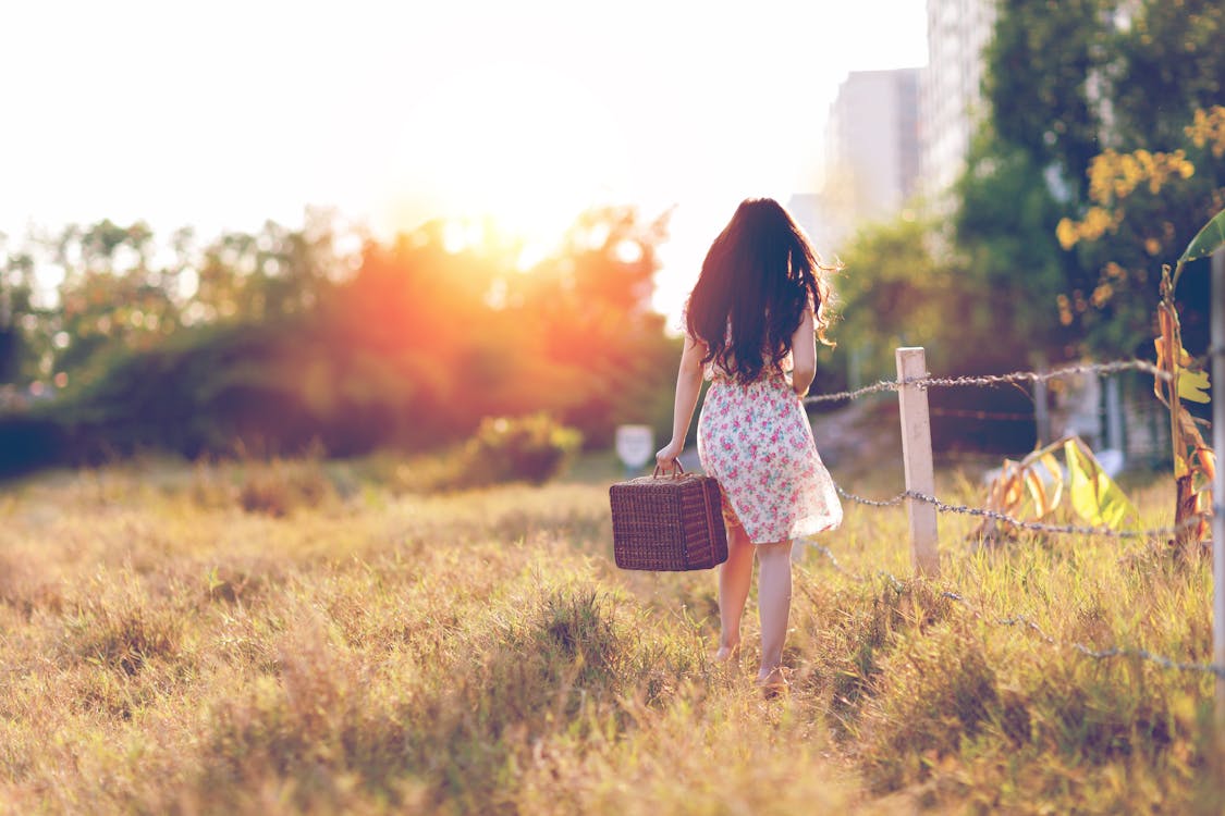 Free Woman in Brown Floral Dress Walking Near Fence Stock Photo