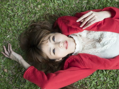 Woman in White Shirt Wearing Red Blazer Lying on Green Grass