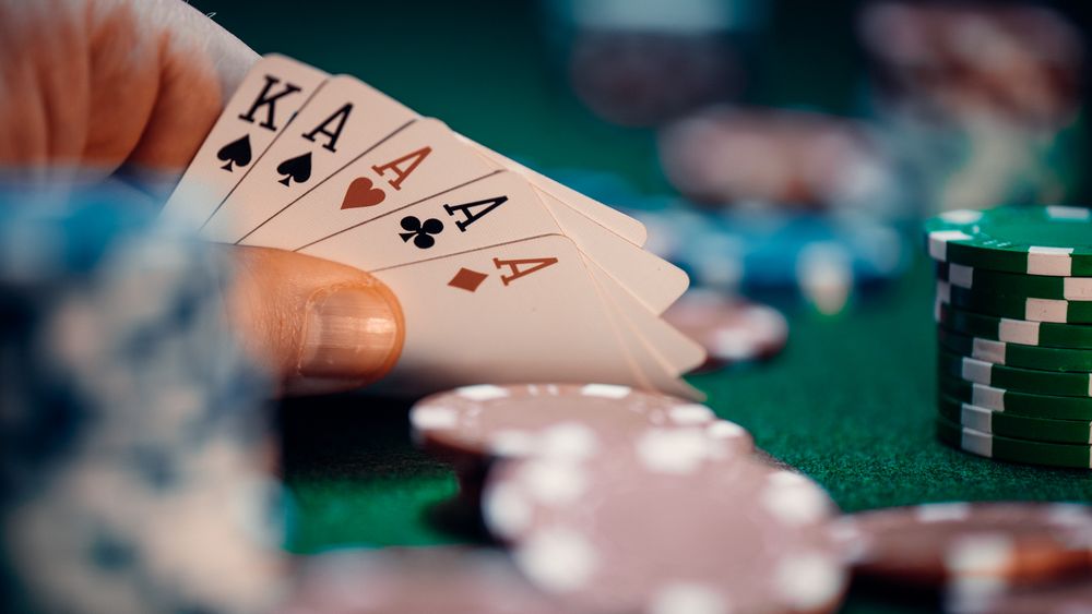 Hand holding playing cards with colorful poker chips scattered on green felt