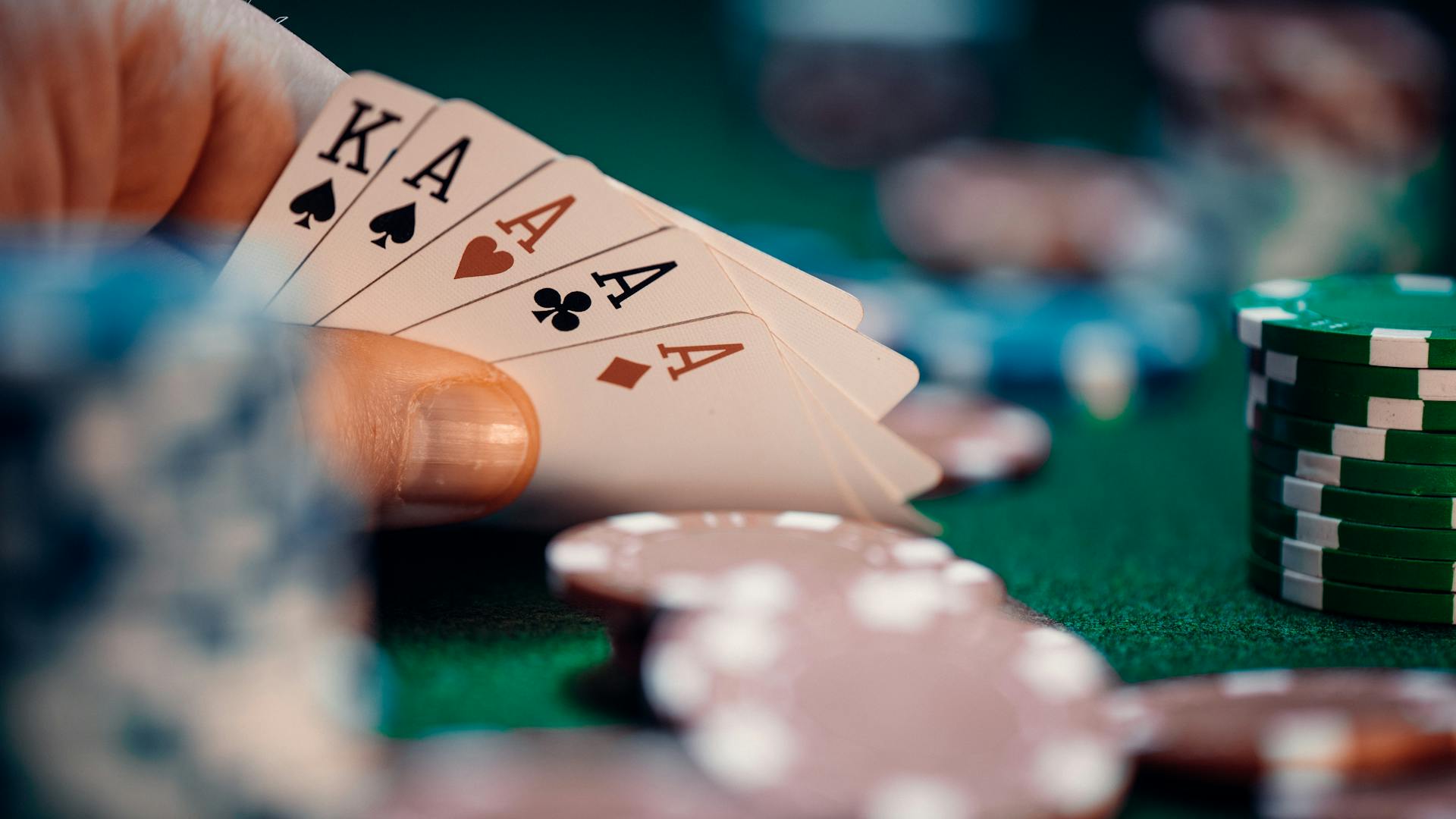 Close-up of poker hand holding four aces and kings with colorful chips on green table for high-stakes gaming.