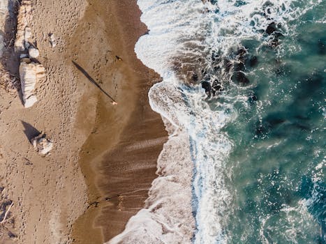 Drone shot of Cambria beach, capturing waves and sandy shore in a beautiful seascape.