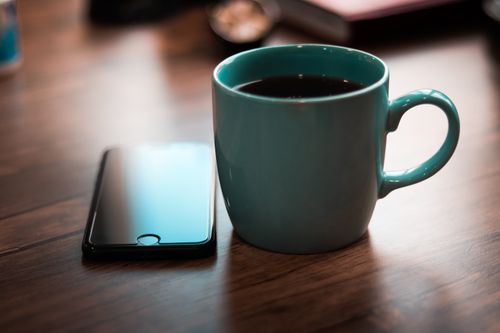 Free A coffee mug and smartphone on a wooden table, capturing a cozy and modern atmosphere. Stock Photo