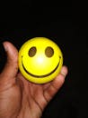 黑色背景下，一只拿着黄色笑脸压力球的手的特写
