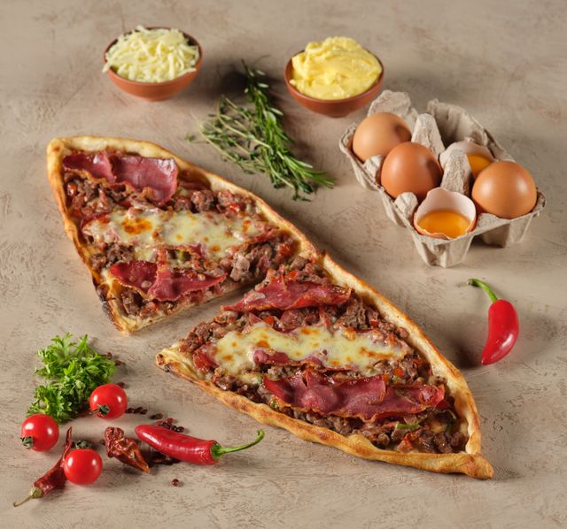 Close-up of Turkish pide garnished with eggs, cheese, and herbs. A flavorful culinary treat.