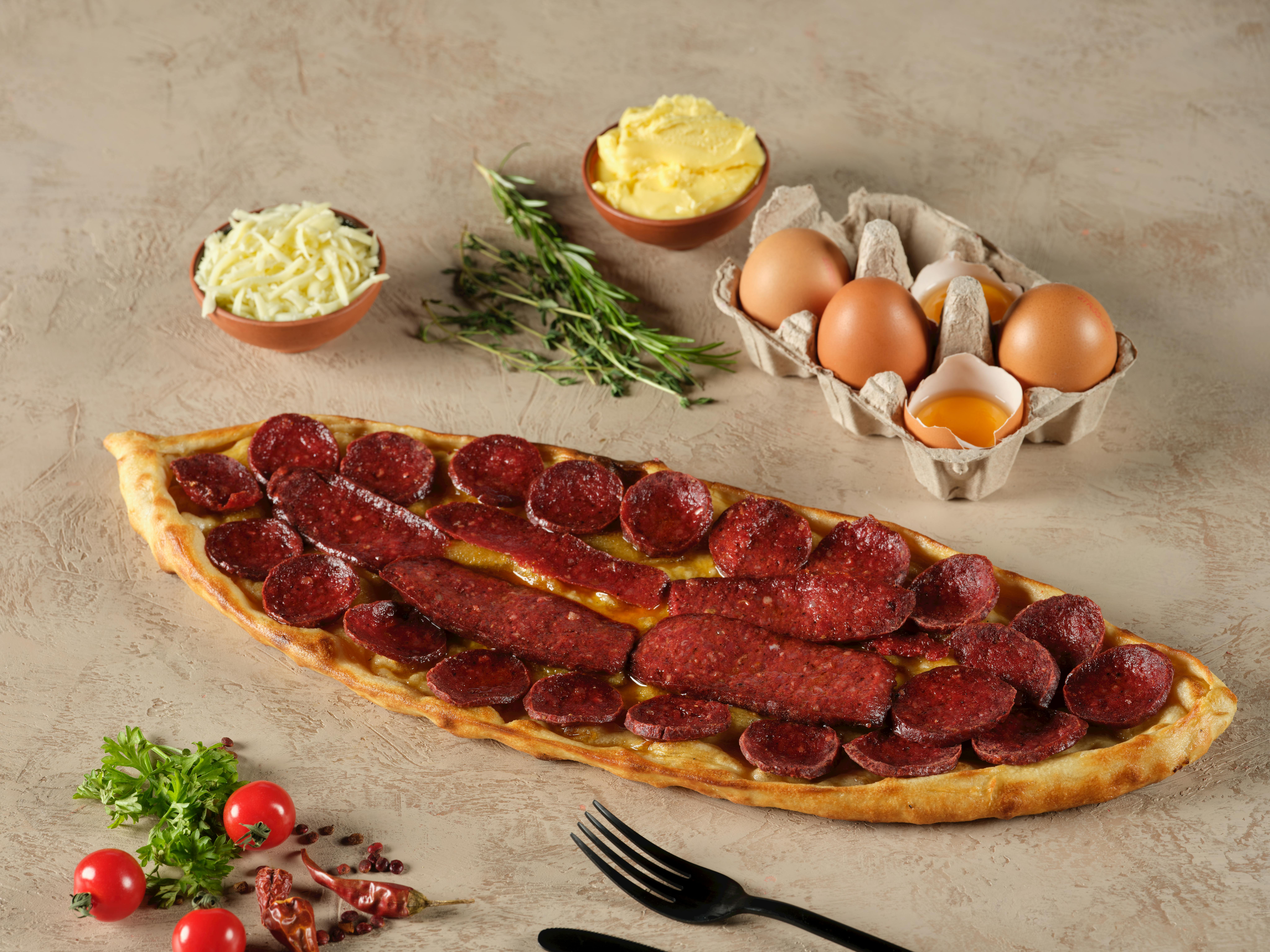 Explore a mouthwatering Turkish pide topped with salami, herbs, and surrounded by ingredients.