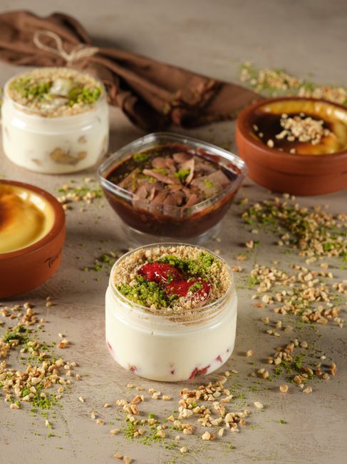 A glass jar of thick chocolate protein pudding topped with sliced banana and crushed almonds, with a spoon resting on the side.