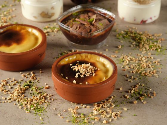 Clay pots of creamy milk pudding with browned tops sprinkled with chopped hazelnuts and pistachio