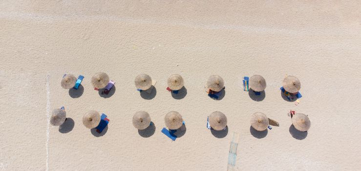 Top view of beach umbrellas casting shadows on sand. Sunlit and serene coastal scene.