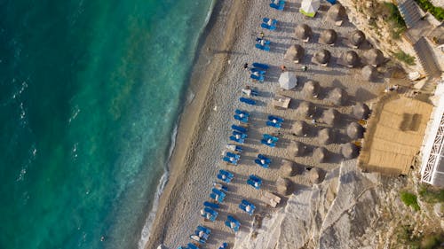 Aerial Footage of a Turquoise Sea and Rows of Sunshades on a Sandy Beach
