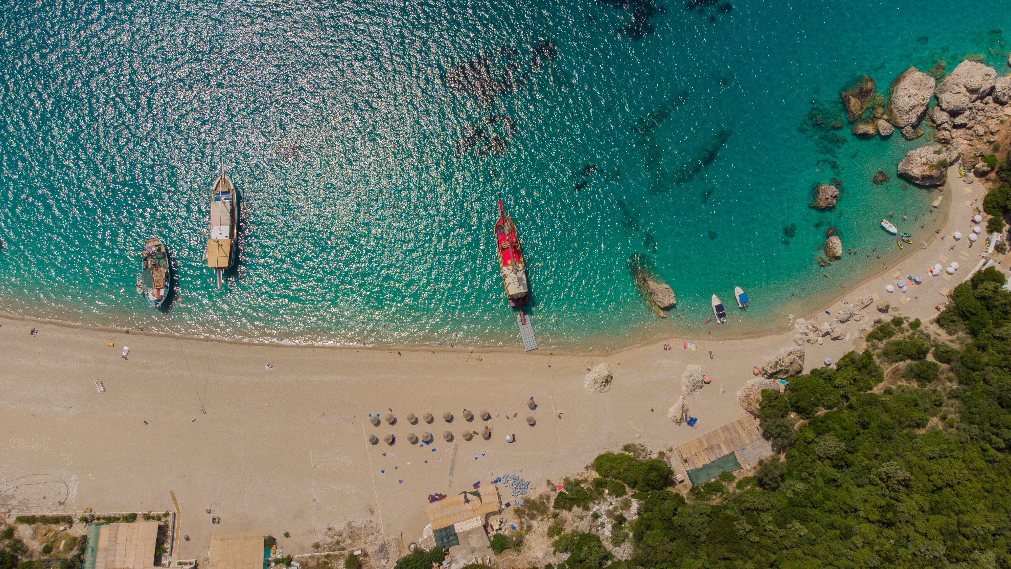 Stunning aerial shot of a sunny beach with boats and vibrant turquoise waters, perfect for summer travel inspiration. - Photo by Amel Uzunovic on Pexels