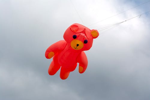 Red Teddy Bear Balloon Floating against a Gray Sky