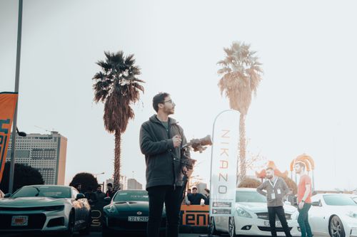 Free Photographer with camera amidst parked cars and palm trees at a sunny event. Stock Photo
