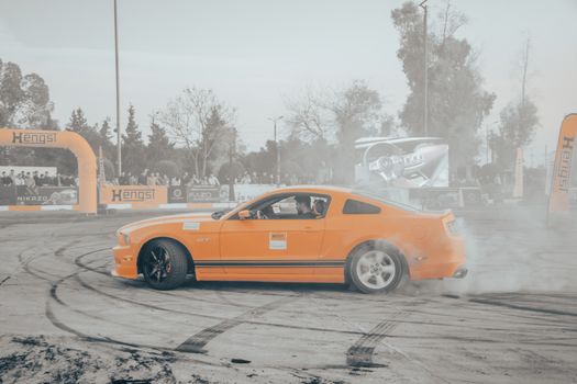 Exciting drifting performance of an orange sports car at a public motorsport event with smoke effects.