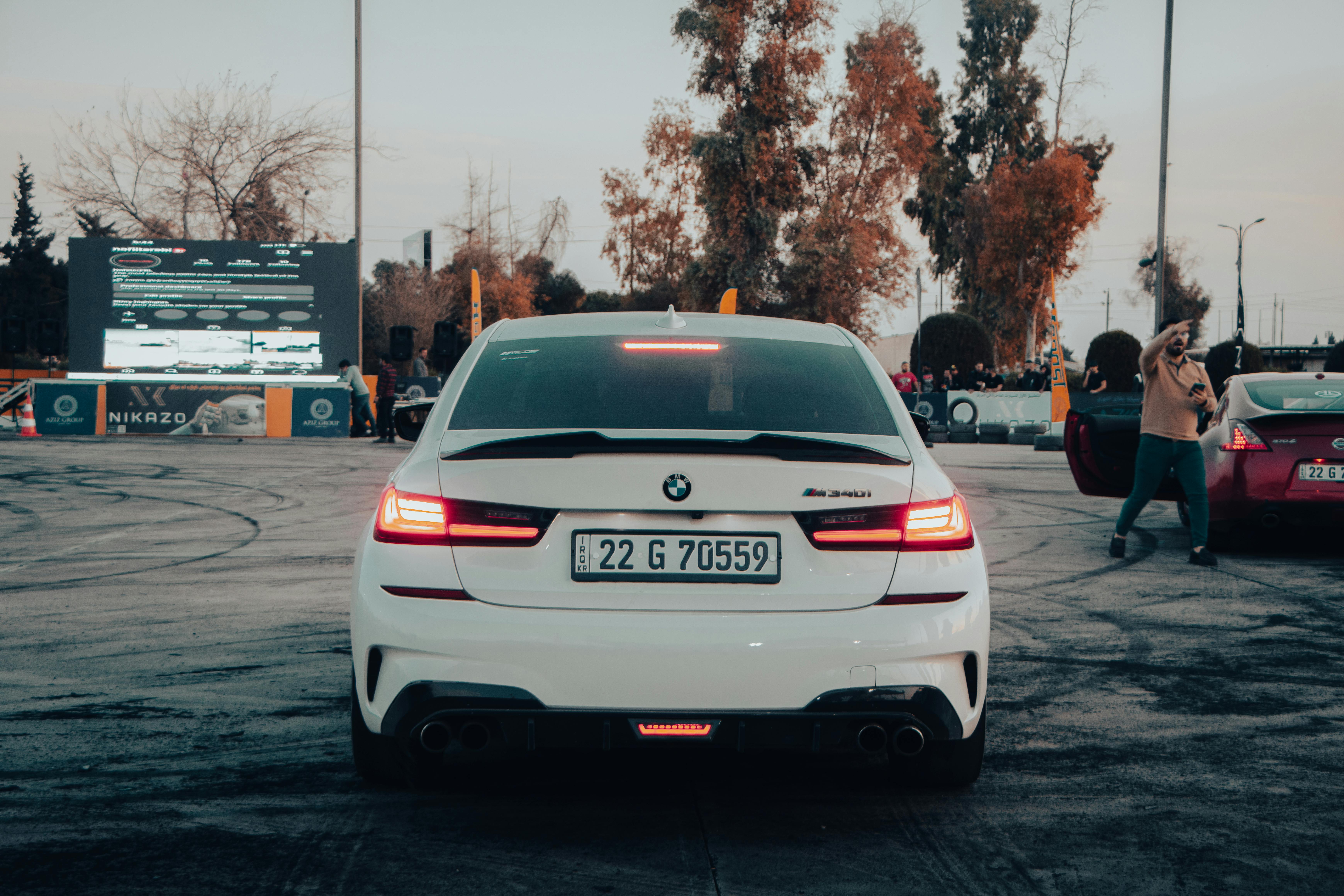 Rear view of a BMW M340i at a car event with people and a screen in twilight settings.