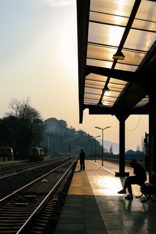 Free A peaceful train station scene with silhouettes and a warm sunset glow. Stock Photo