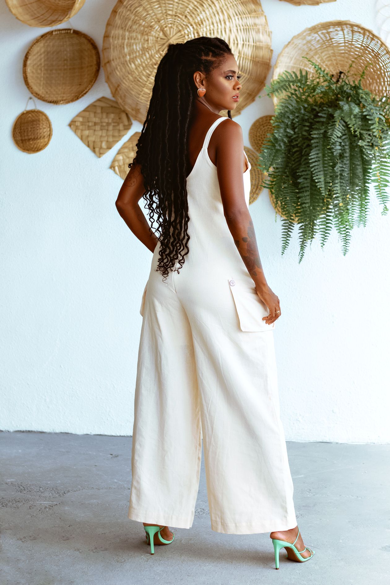 Woman in a white wide-leg jumpsuit with green heeled sandals.