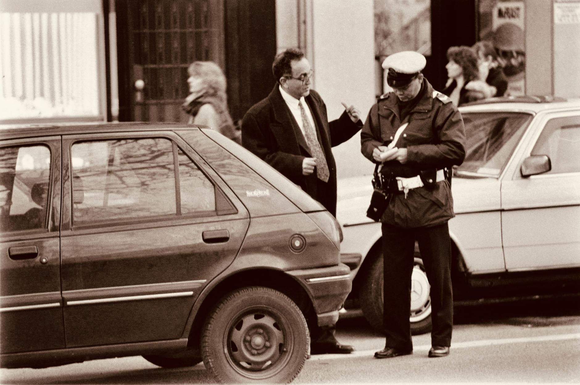 A police officer issues a parking ticket to a driver on a busy city street. Sepia-toned.