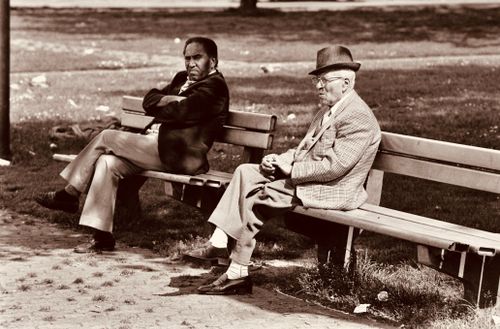 Free Two senior men sitting on benches in a park, chatting in vintage attire. Stock Photo