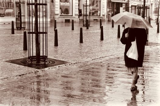 Woman with umbrella walking on a wet city sidewalk in sepia tone.
