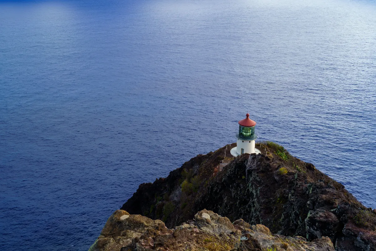 Makapuu Point Lighthouse with its red roof on the cliff below the Oahu lookout trail