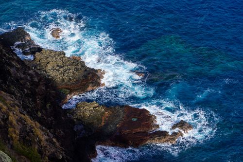 Free High-angle aerial view of waves crashing against rugged cliffs, displaying rich blue hues. Stock Photo