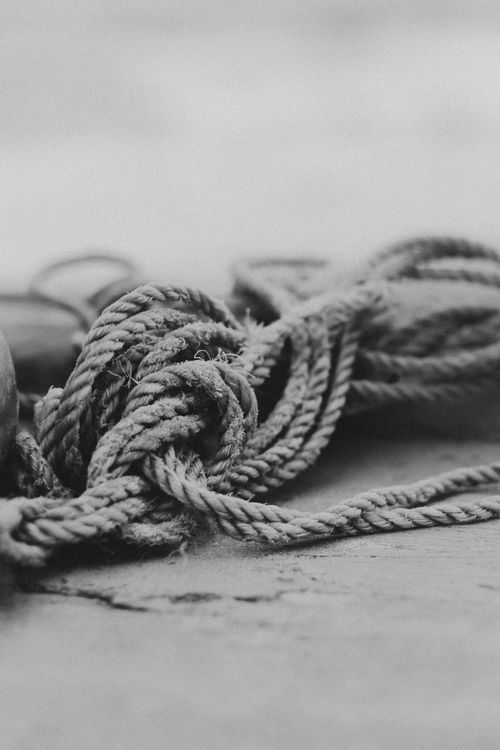 Free Monochrome shot of a detailed nautical rope knot laying on sand, evoking a sense of maritime adventure. Stock Photo