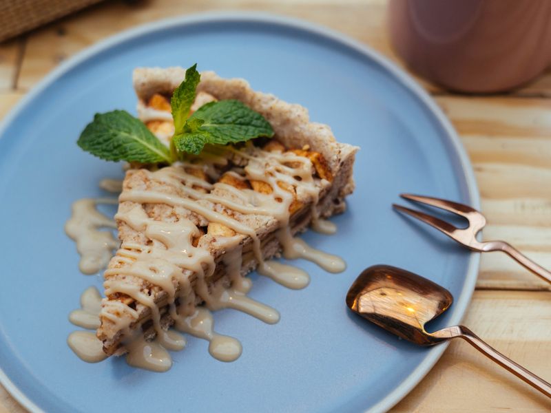A mouthwatering slice of apple tart with caramel drizzle on a blue plate, garnished with m