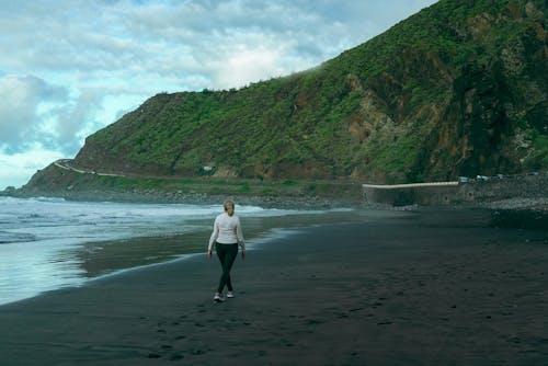 Woman Walking on Beach with Hill with Trees behind