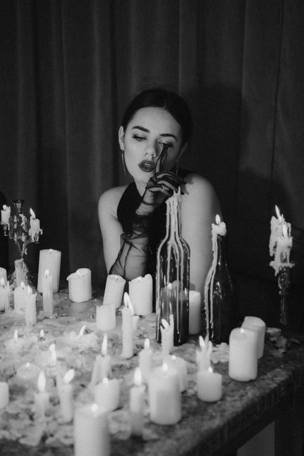 A young woman sitting among numerous candles and bottles, creating a moody atmosphere.