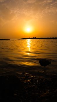 Serene ocean sunset with golden reflections on the water and a distant silhouette island.