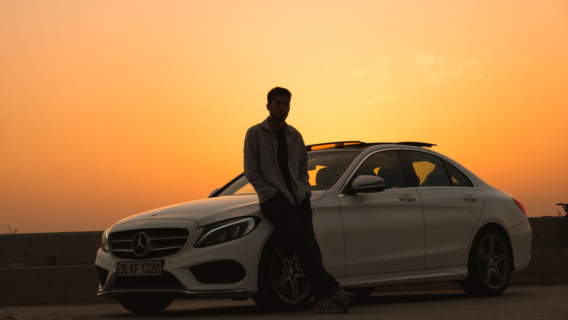 Silhouette of a man leaning on a Mercedes-Benz during a sunset, symbolizing luxury and relaxation.