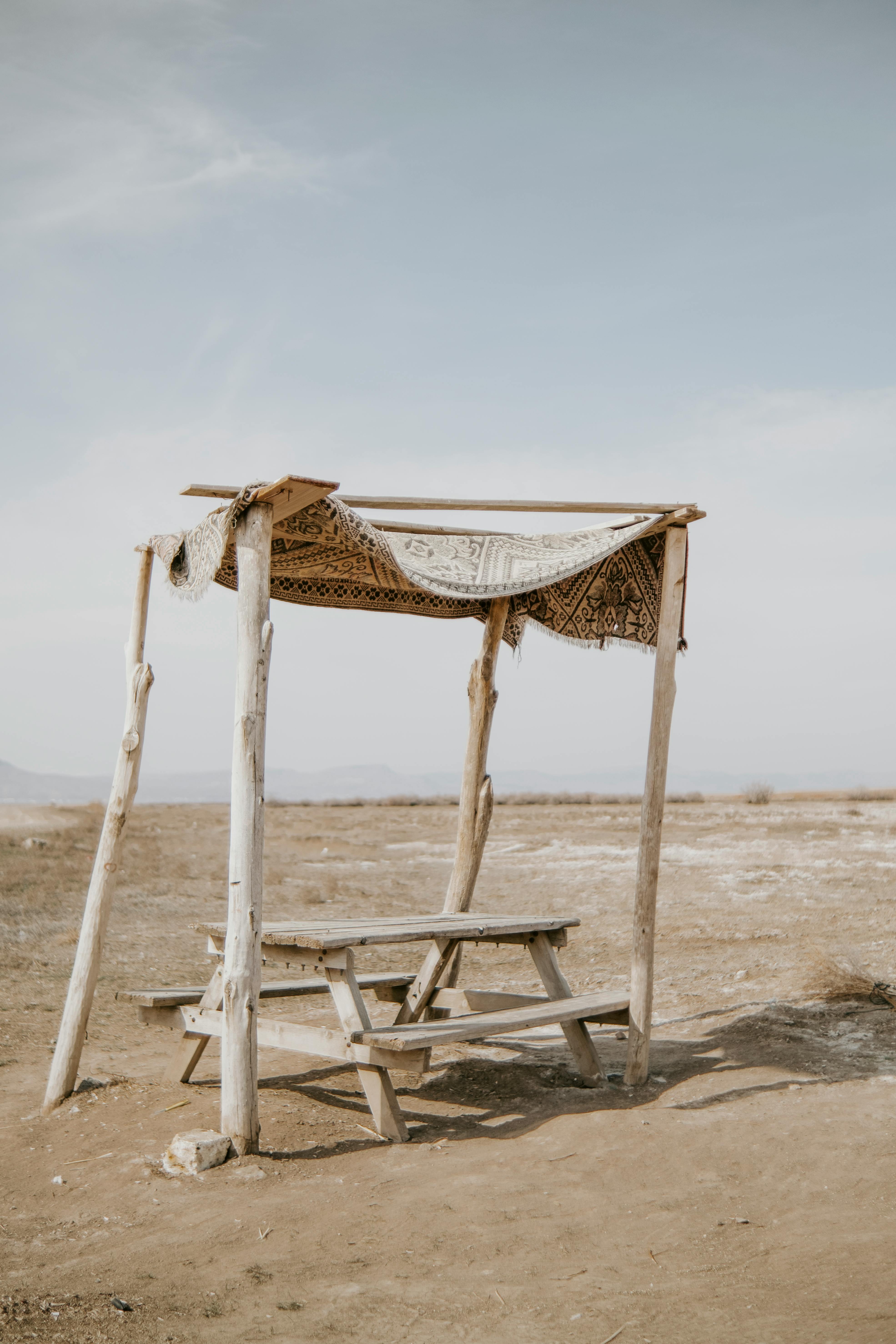 Desolate landscape with a rustic wooden shelter and picnic table under a blue sky.