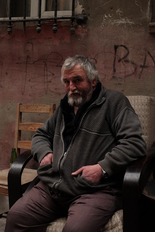 Free A senior man sitting on an armchair in an urban street setting with graffiti in the background. Stock Photo