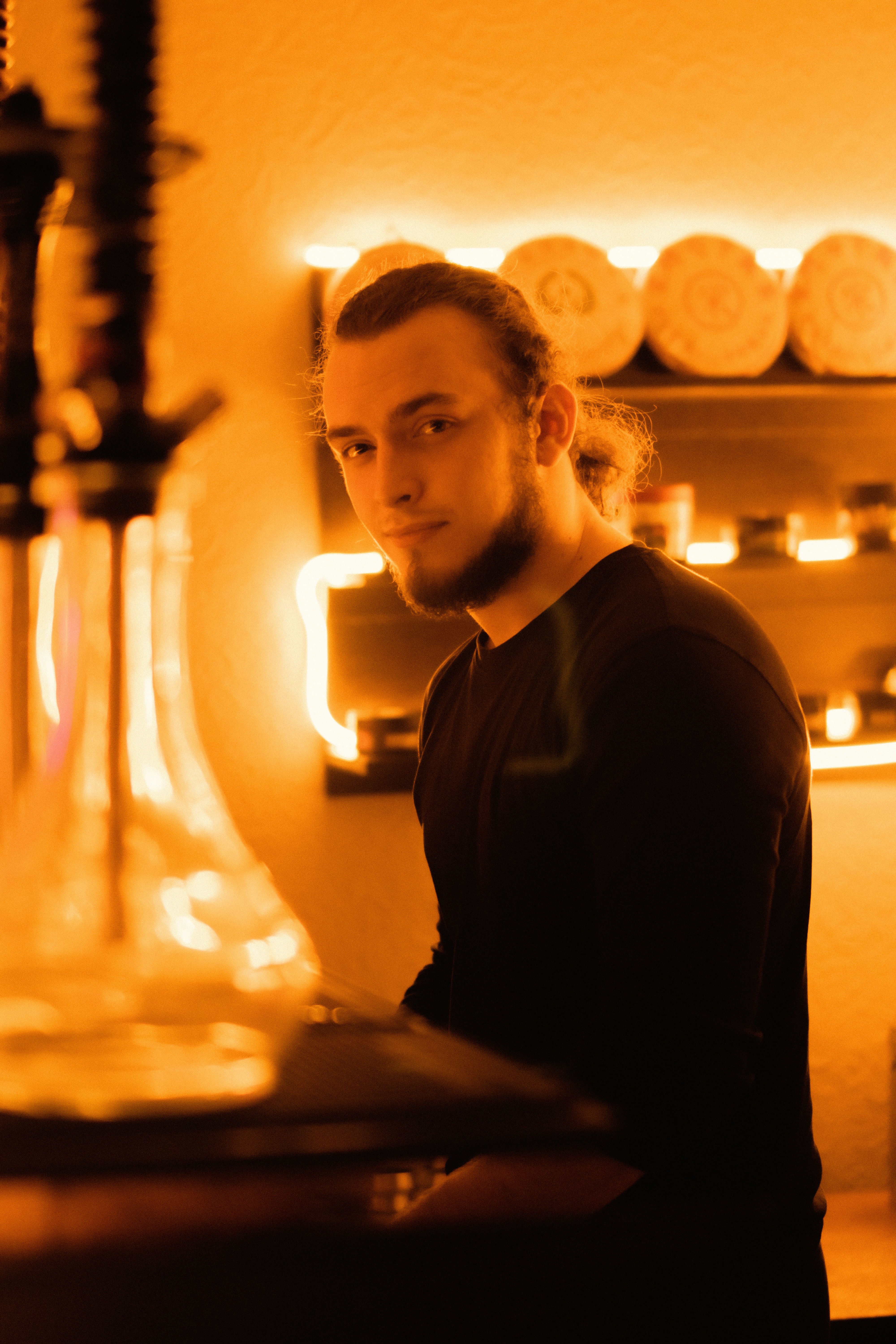 A young man with a beard in a warmly lit setting, creating a cozy ambiance.