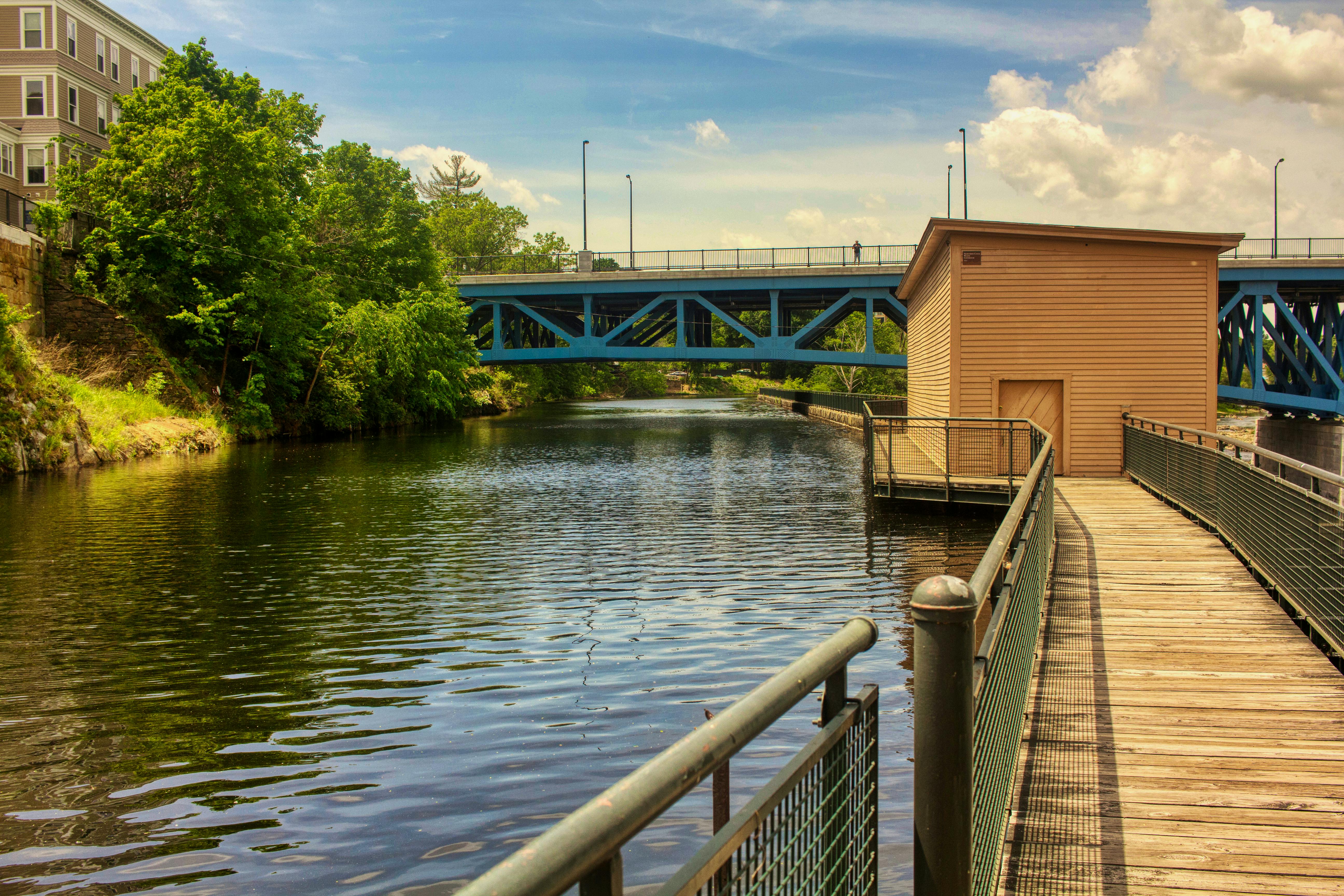 Tranquil urban canal scene with a blue bridge and wooden walkway on a sunny day.