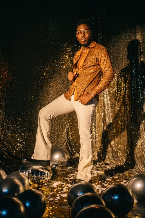Free Man in retro outfit posing with balloons and glitter backdrop at a disco-themed party. Stock Photo