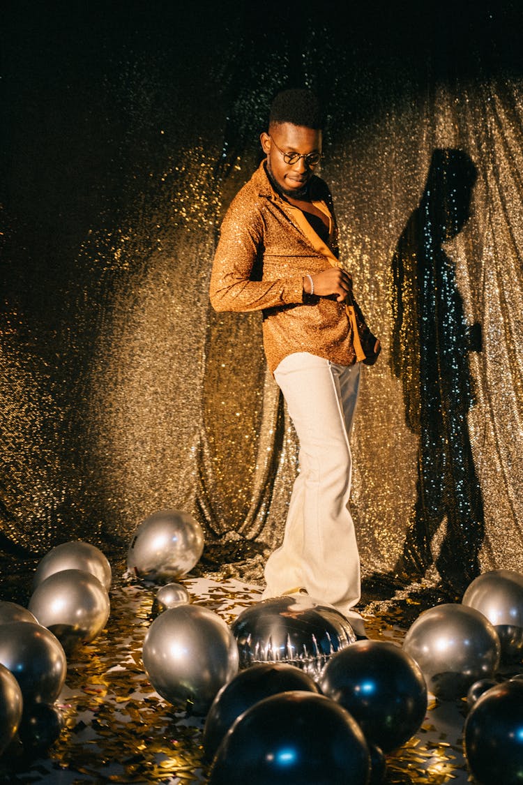 Man In Gold Shirt Standing In Front Of Glittering Curtain