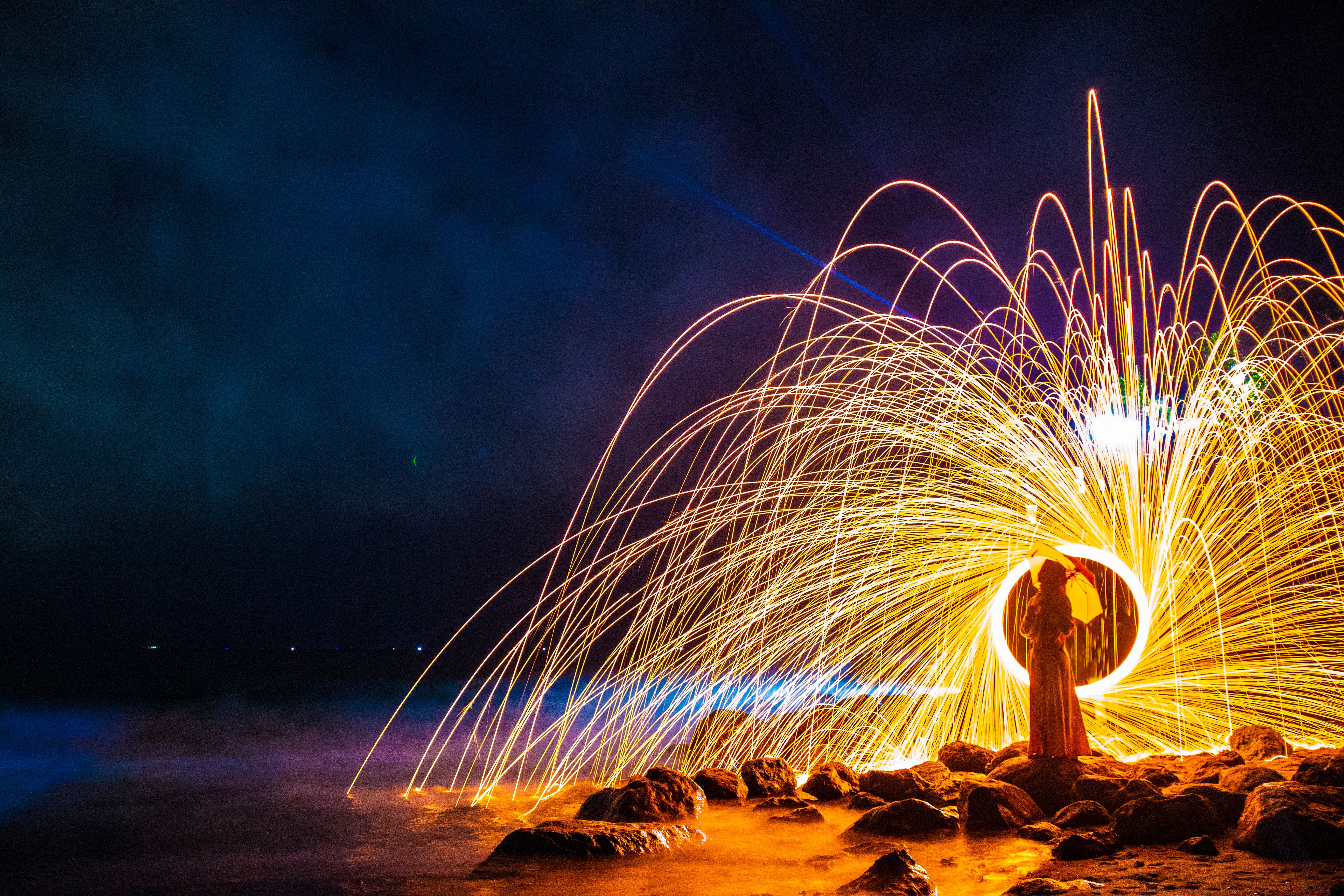 A captivating fireworks display on a rocky beach in Lombok, Indonesia, with a silhouette in the foreground.