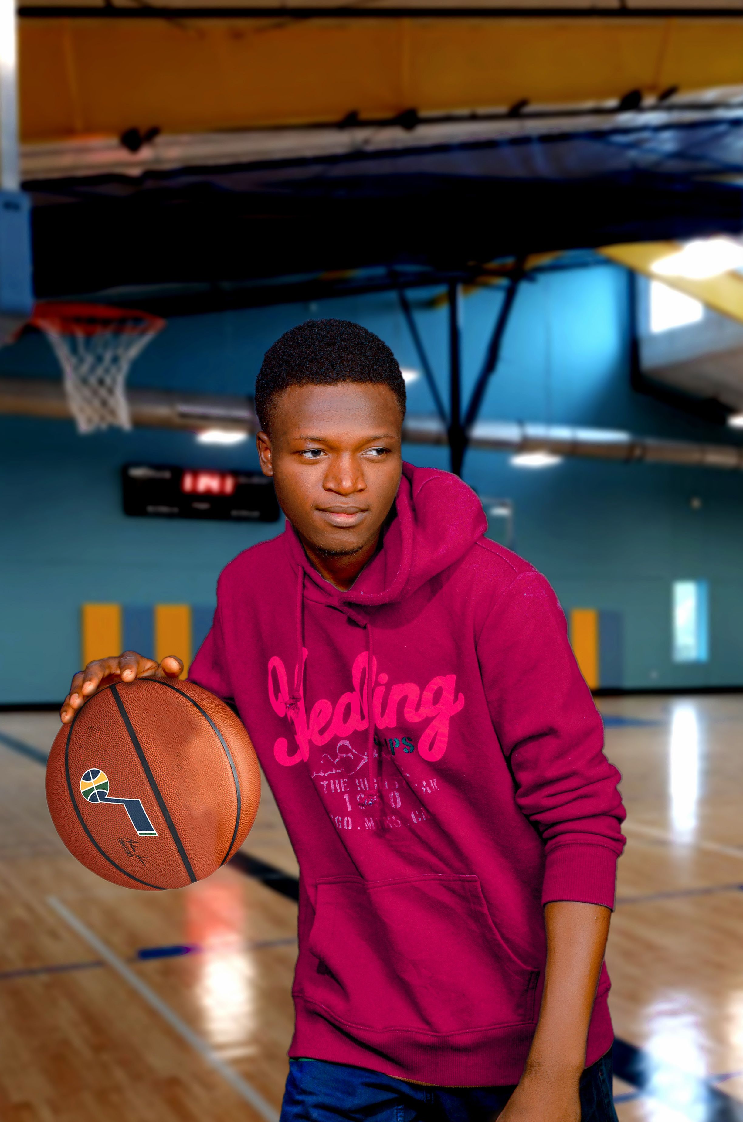 Portrait of a young man in a hoodie holding a basketball on an indoor court.